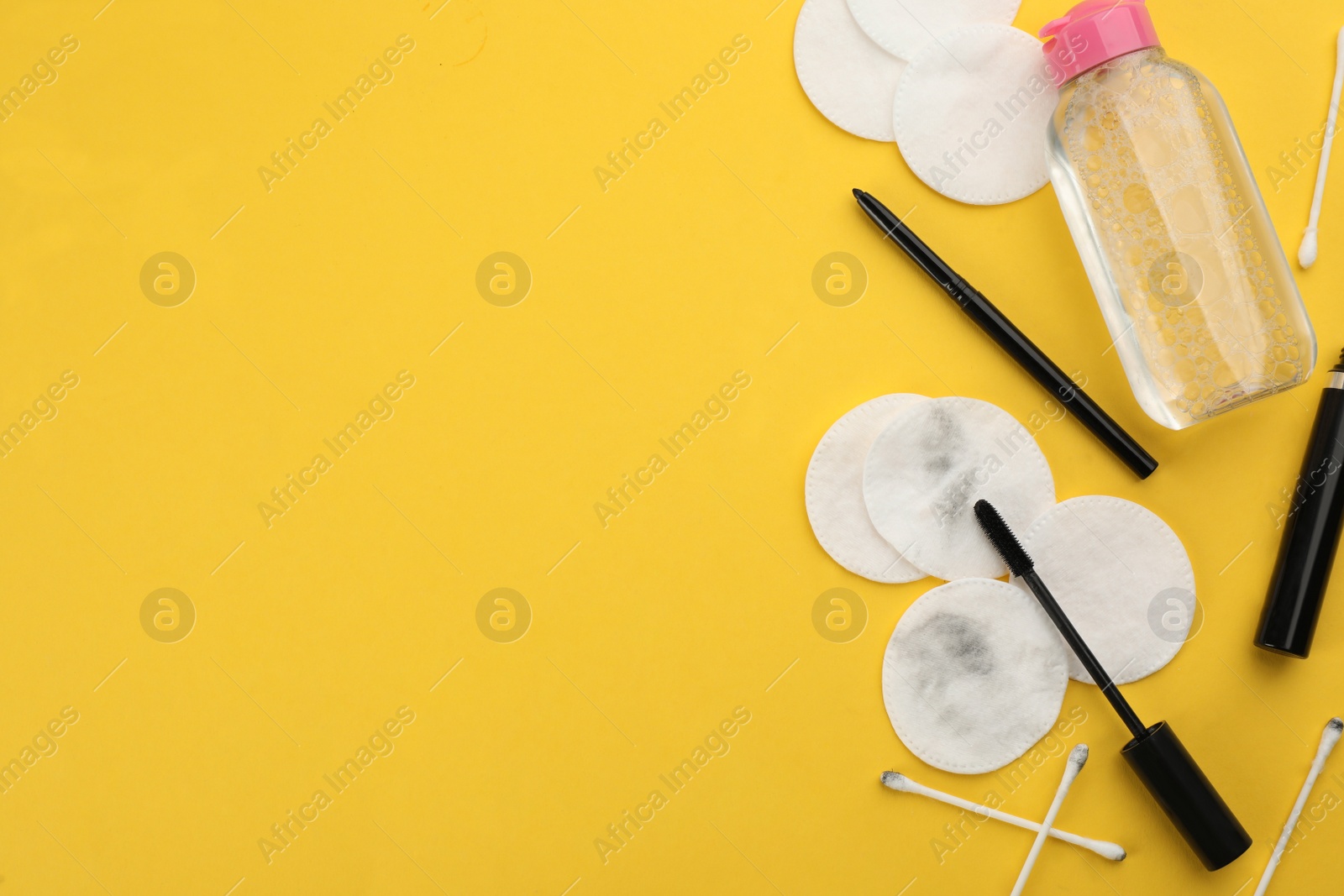 Photo of Dirty cotton pads, swabs, mascara and micellar cleansing water on yellow background, flat lay. Space for text