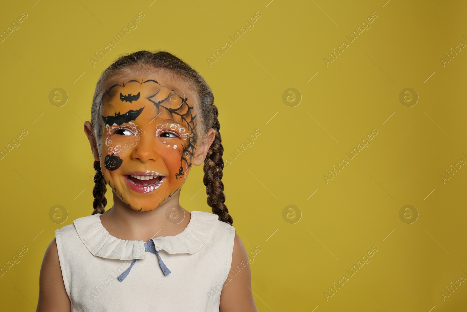 Photo of Cute little girl with face painting on orange background. Space for text