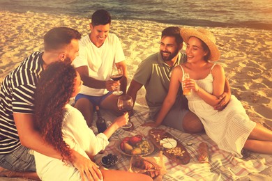 Image of Group of friends having picnic on sandy beach near sea
