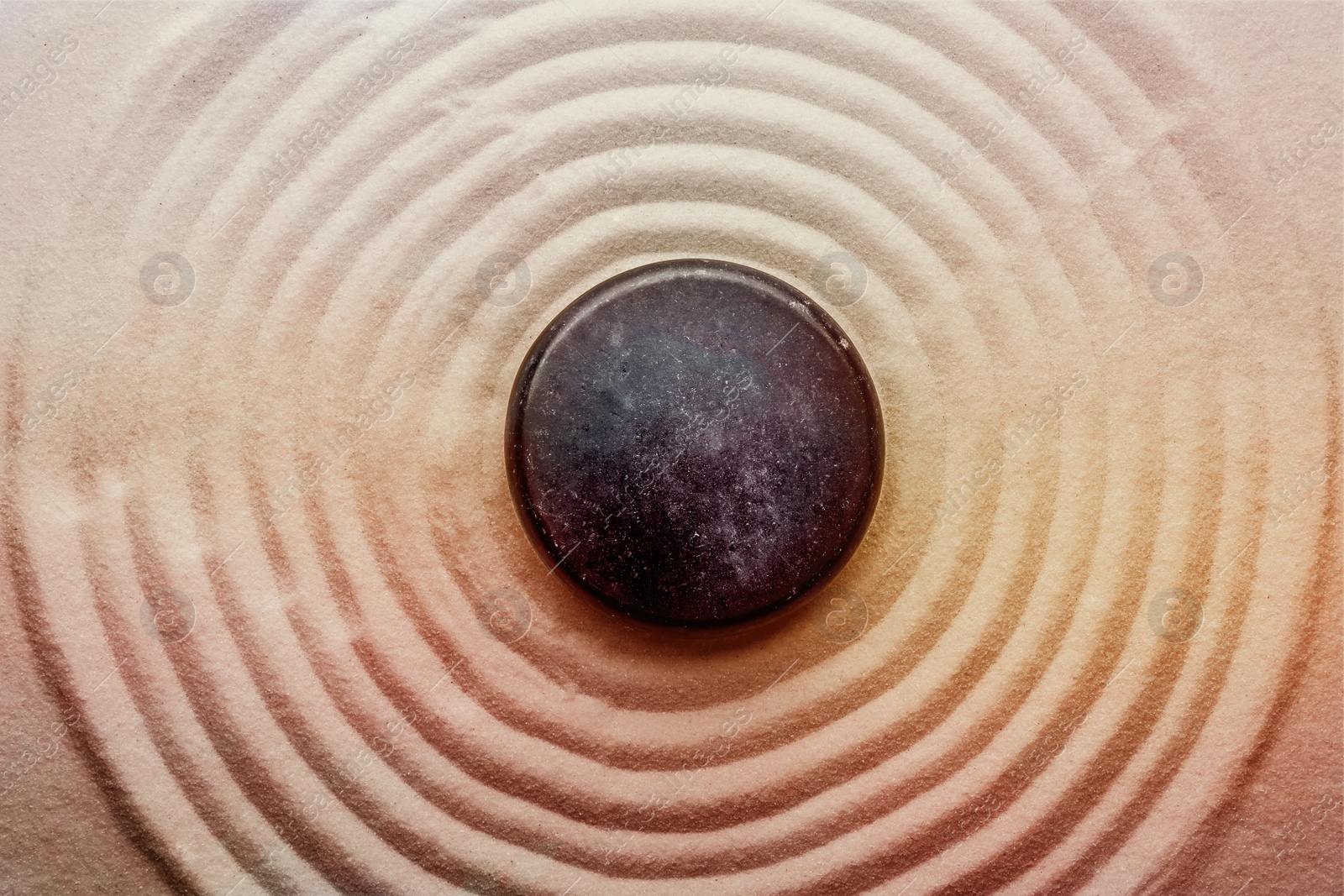 Image of Black stone on sand with pattern, top view. Zen, meditation, harmony