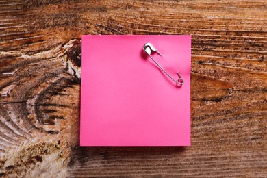 Photo of Pink paper note attached with safety pin on wooden table, top view. Space for text