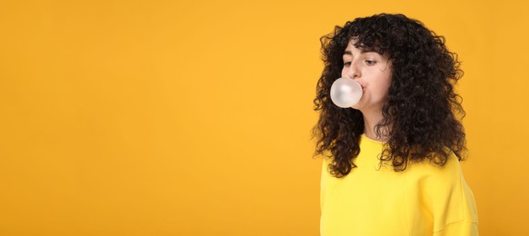 Beautiful young woman blowing bubble gum on orange background. Space for text