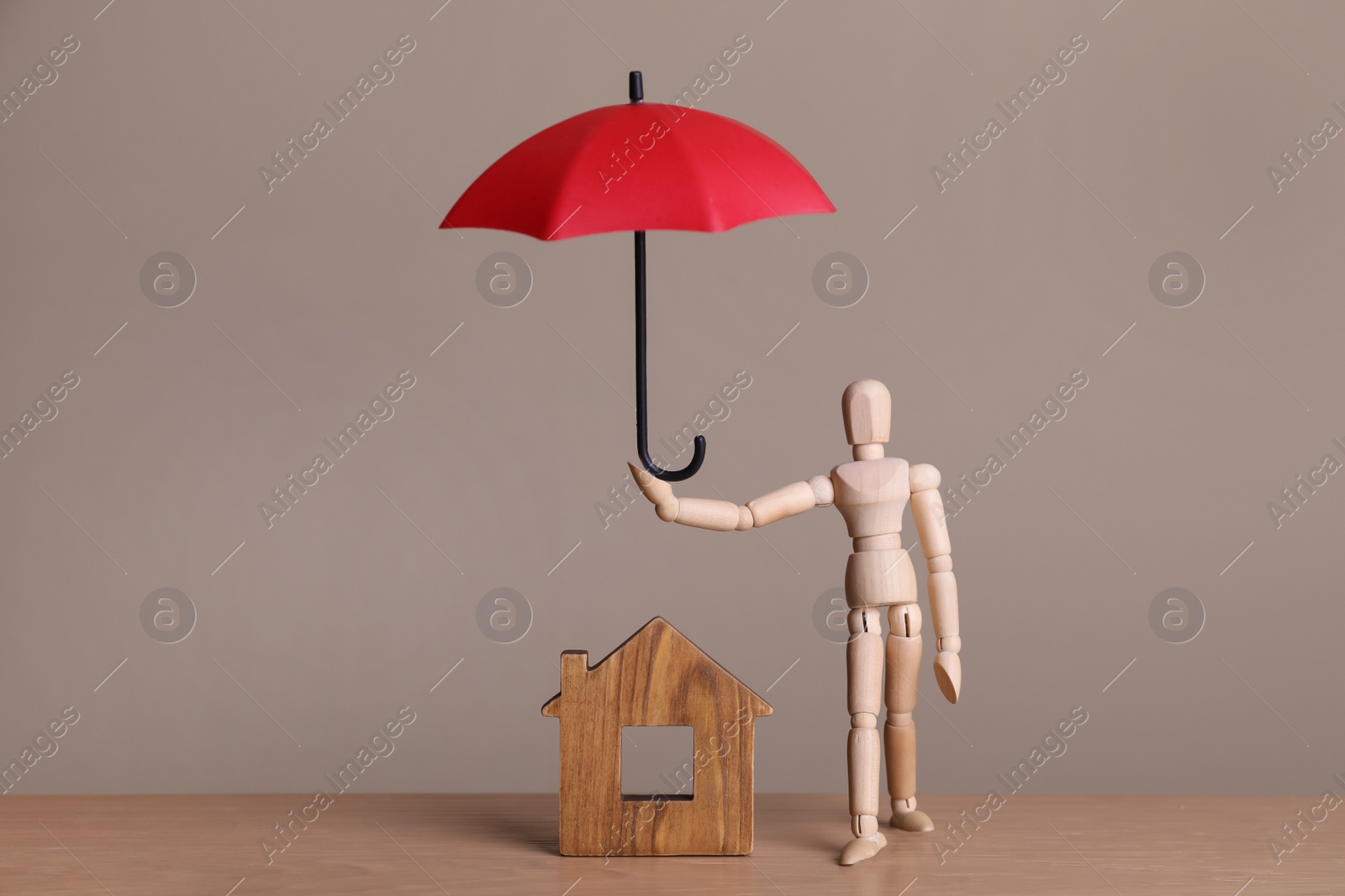 Photo of Mannequin holding small umbrella over house figure on wooden table