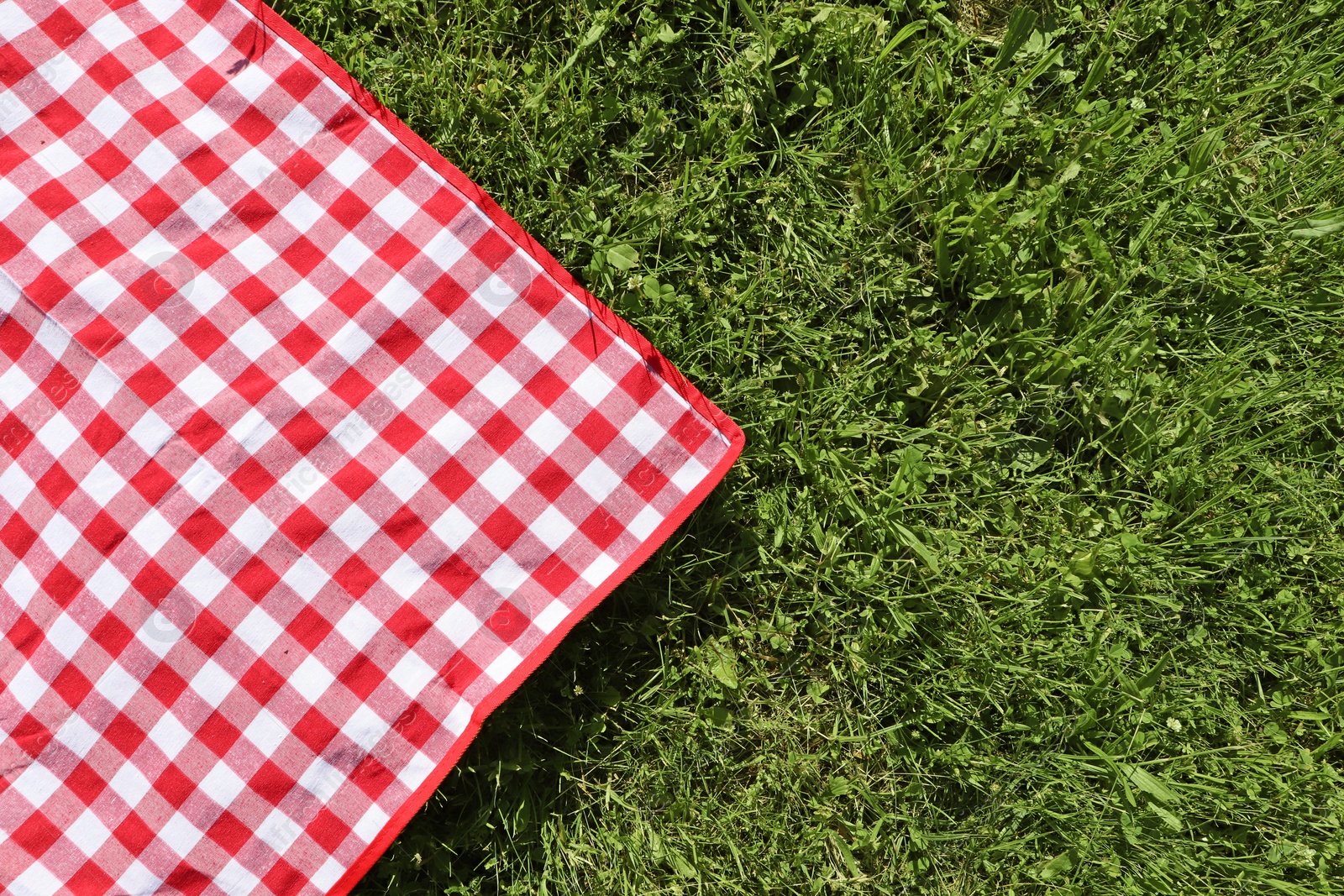 Photo of Checkered picnic tablecloth on fresh green grass, top view. Space for text