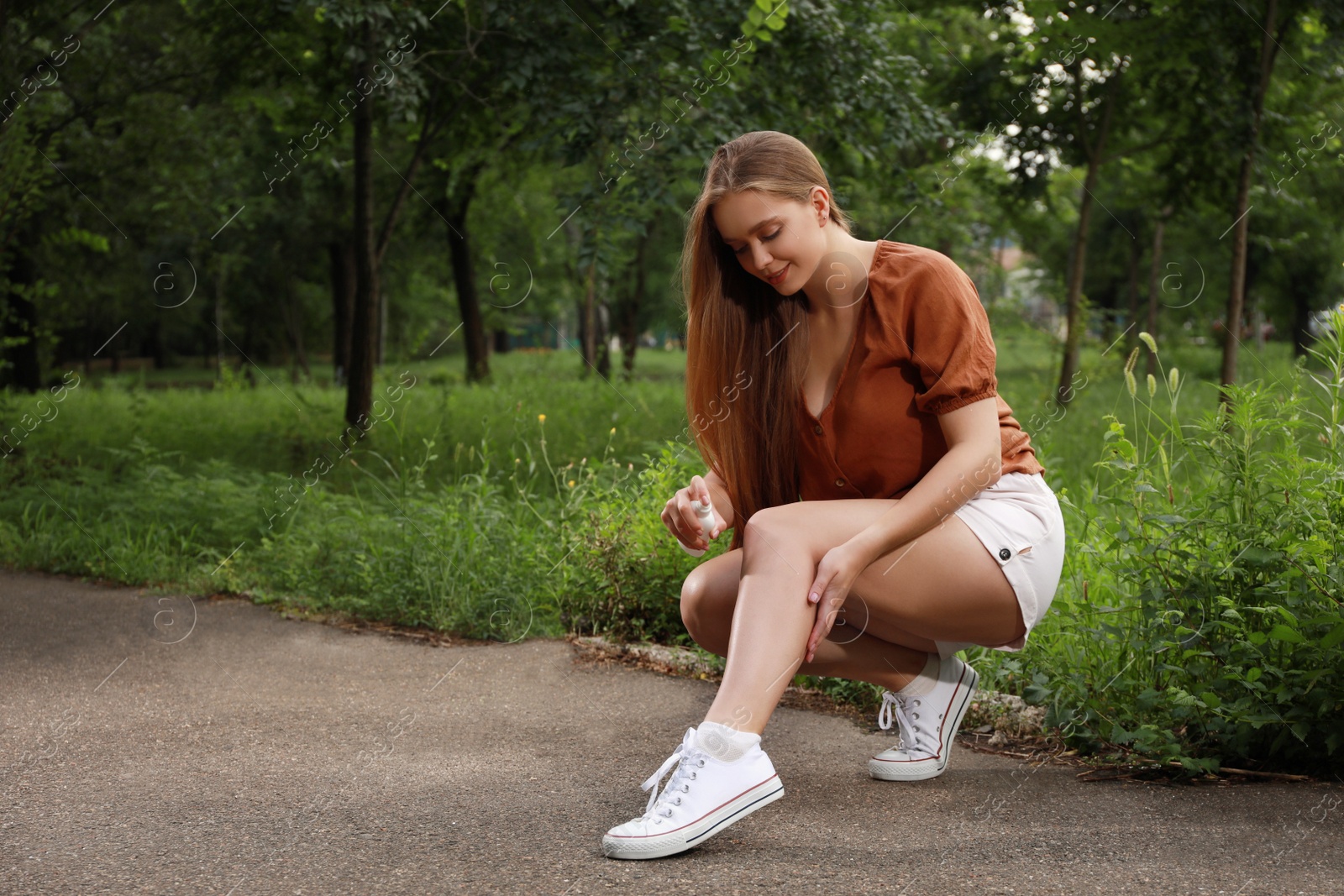 Photo of Woman applying insect repellent onto leg in park. Tick bites prevention