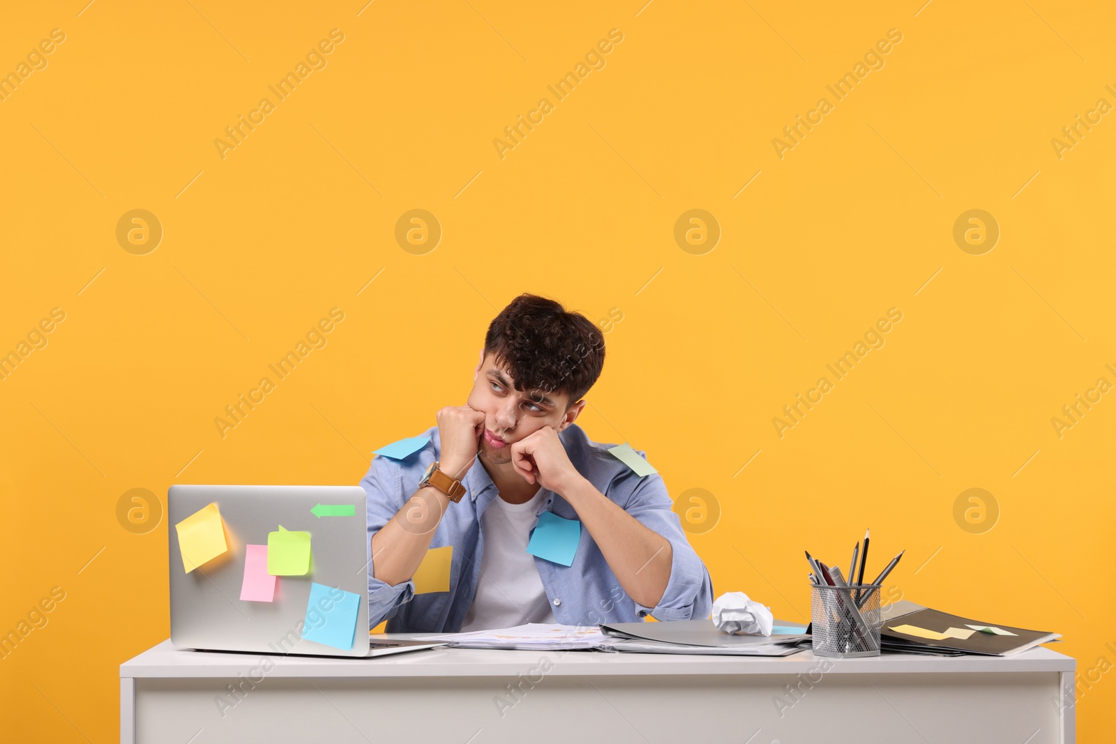 Photo of Tired young man working at white table on orange background. Deadline concept