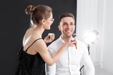Photo of Professional makeup artist working with  young man in photo studio