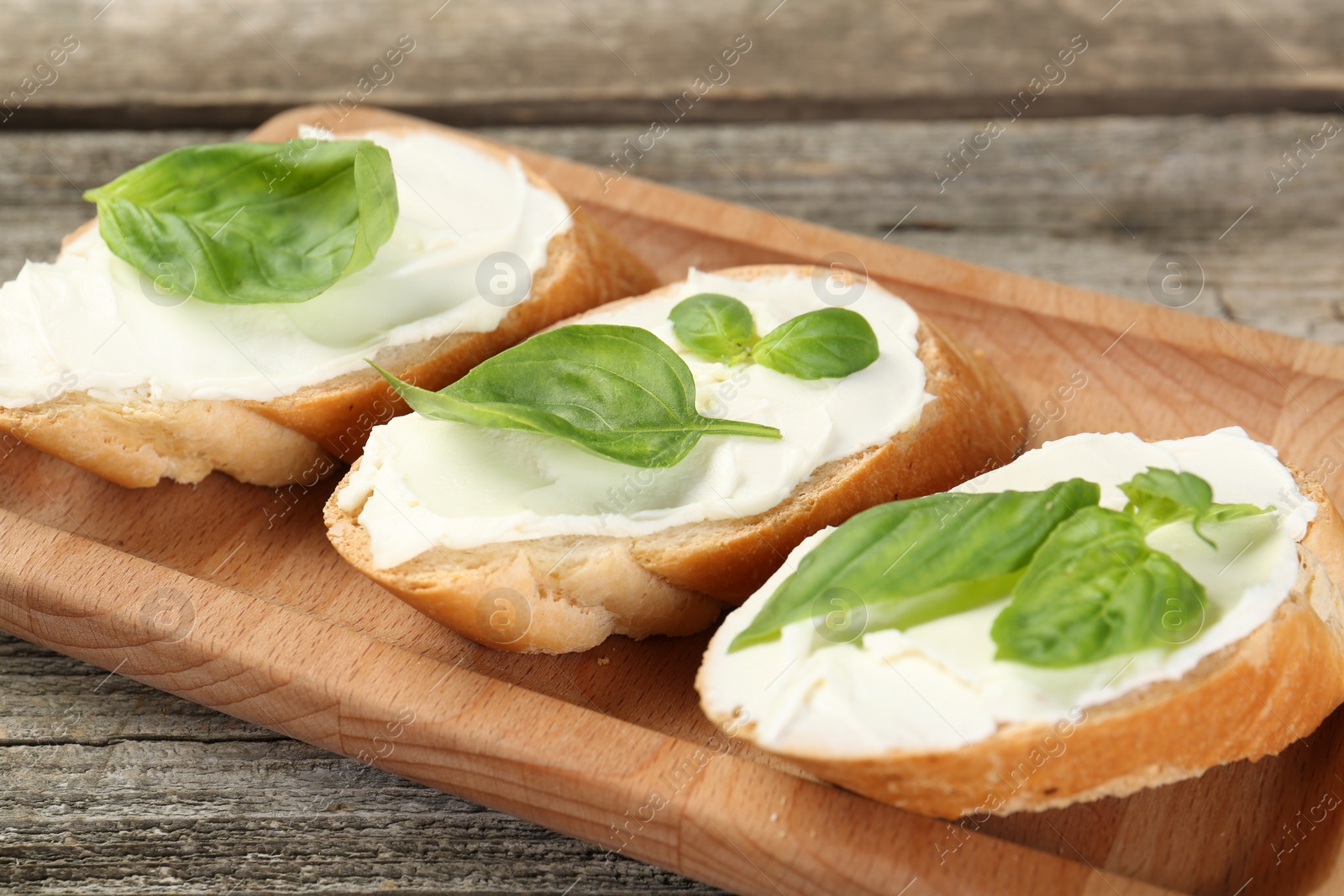 Photo of Delicious sandwiches with cream cheese and basil leaves on wooden table, closeup