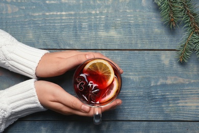 Photo of Woman holding cup with hot mulled wine on table, top view