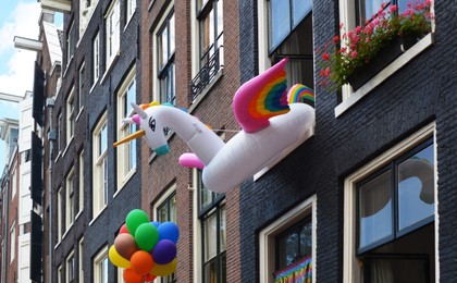 Photo of Inflatable unicorn ring and rainbow balloons on building facade. LGBT pride concept