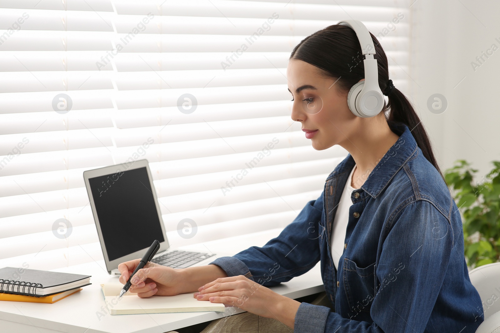 Photo of Online translation course. Student in headphones writing near laptop at home