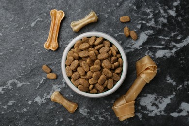 Dry dog food and treats (chew bones) on black textured background, flat lay