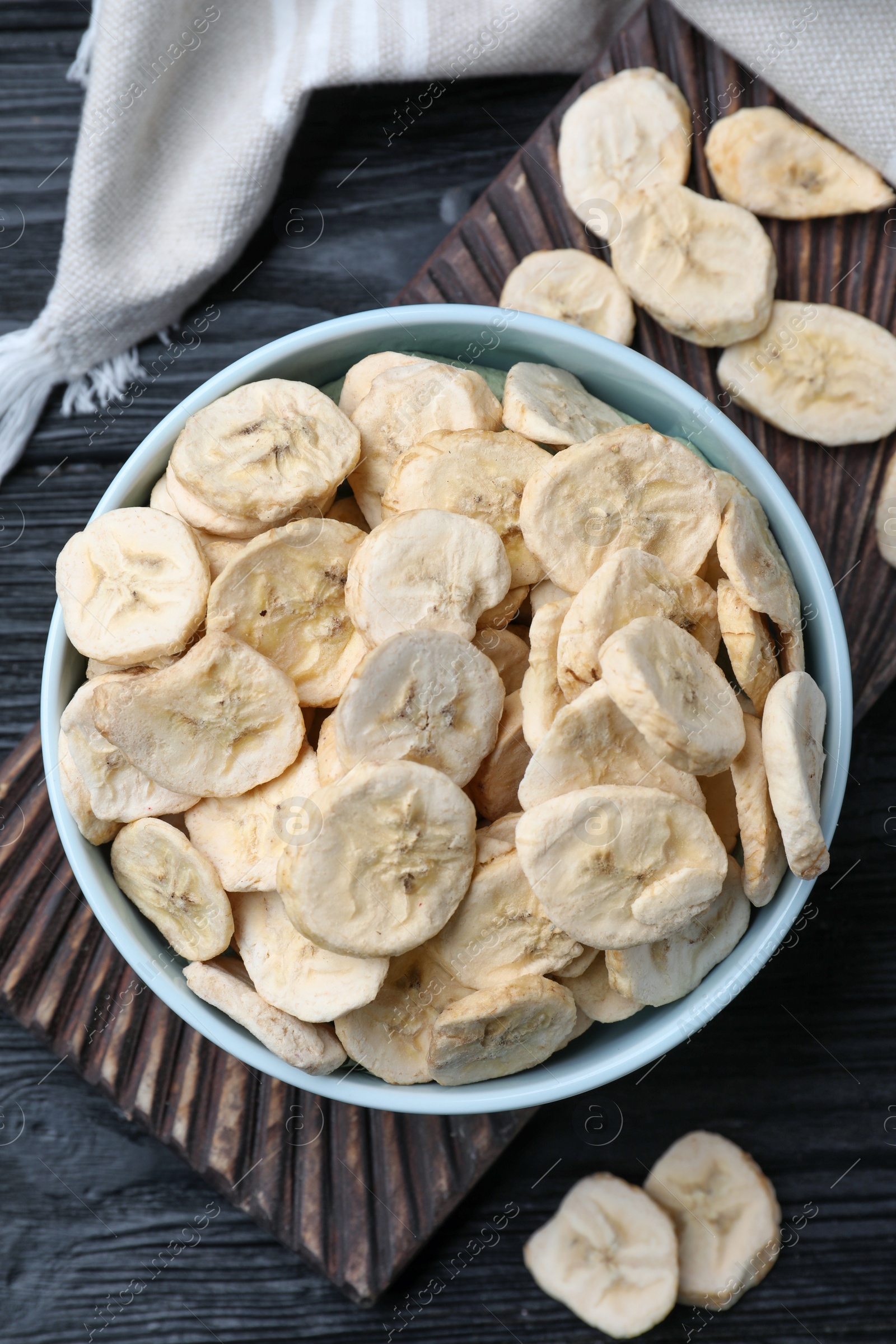 Photo of Bowl and dried banana slices on black wooden table, top view