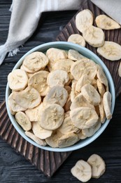 Bowl and dried banana slices on black wooden table, top view