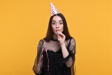 Photo of Woman in party hat with blower and streamers on orange background