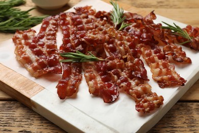 Photo of Slices of tasty fried bacon and rosemary on wooden table, closeup