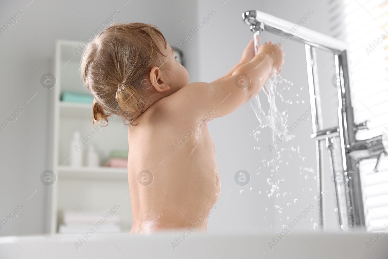 Photo of Cute little girl playing with faucet in bathtub at home