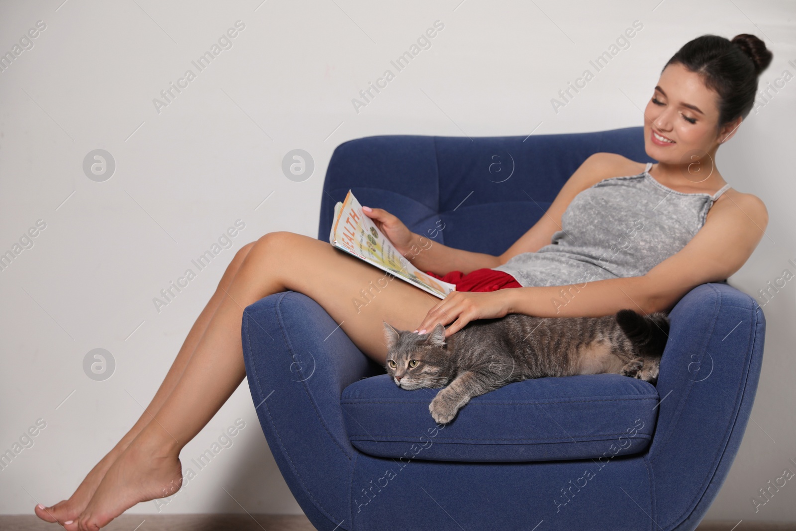 Photo of Young woman with cat and magazine on armchair at home. Cute pet