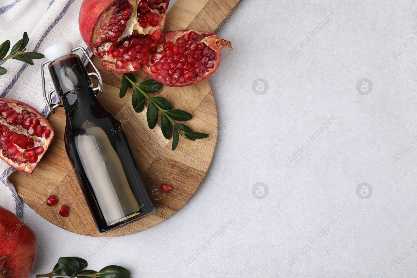 Photo of Tasty pomegranate sauce in bottle, branches and fruits on light table, flat lay. Space for text