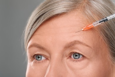 Photo of Senior woman getting facial injection on light grey background, closeup. Cosmetic surgery