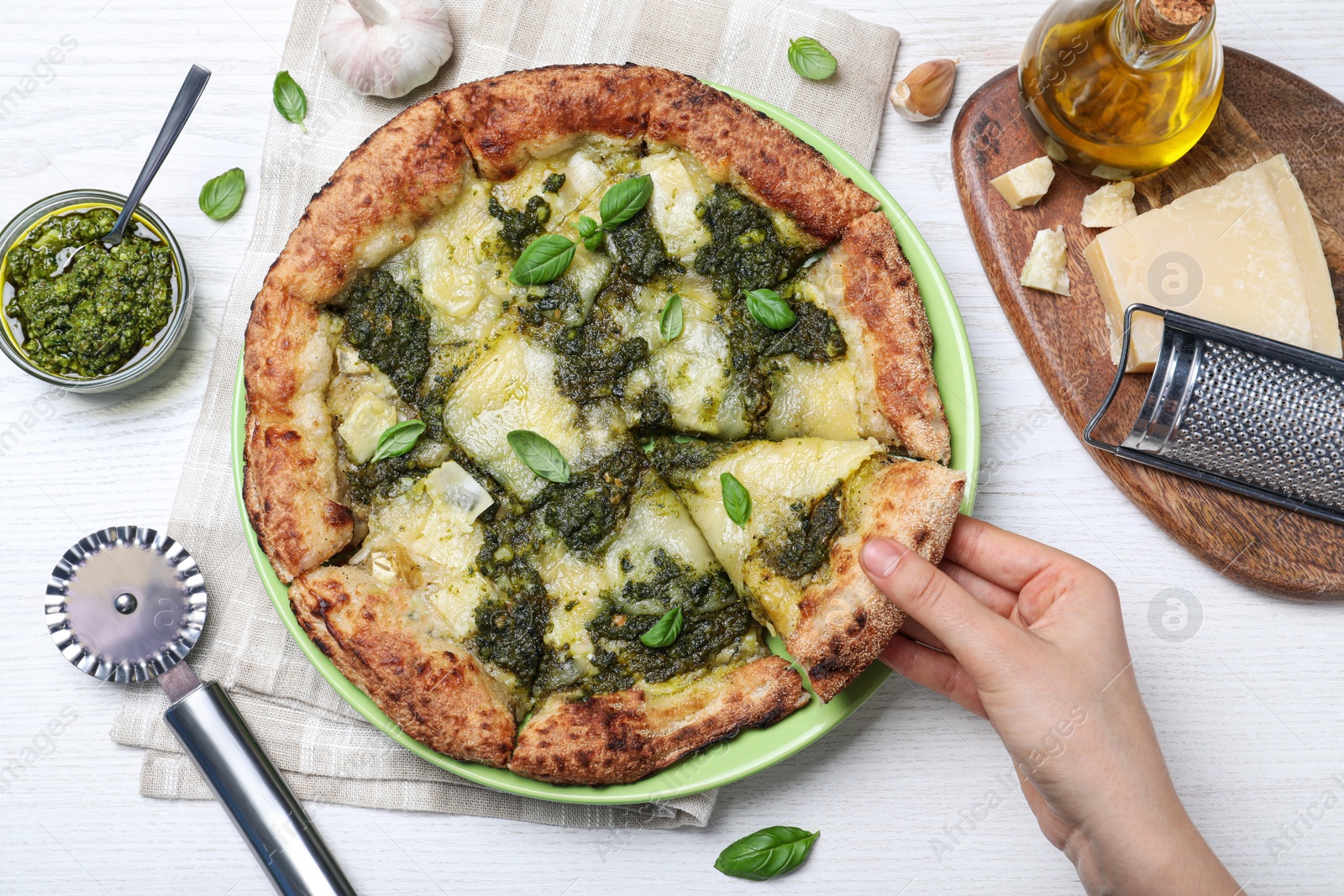 Photo of Woman taking slice of delicious pizza with pesto, cheese and basil at white wooden table, closeup