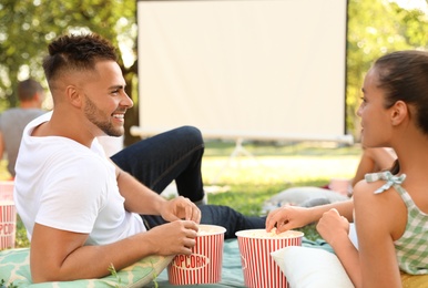 Young couple with popcorn watching movie in open air cinema. Space for text