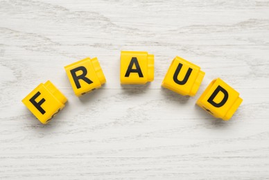 Word Fraud of yellow cubes with letters on white wooden background, flat lay