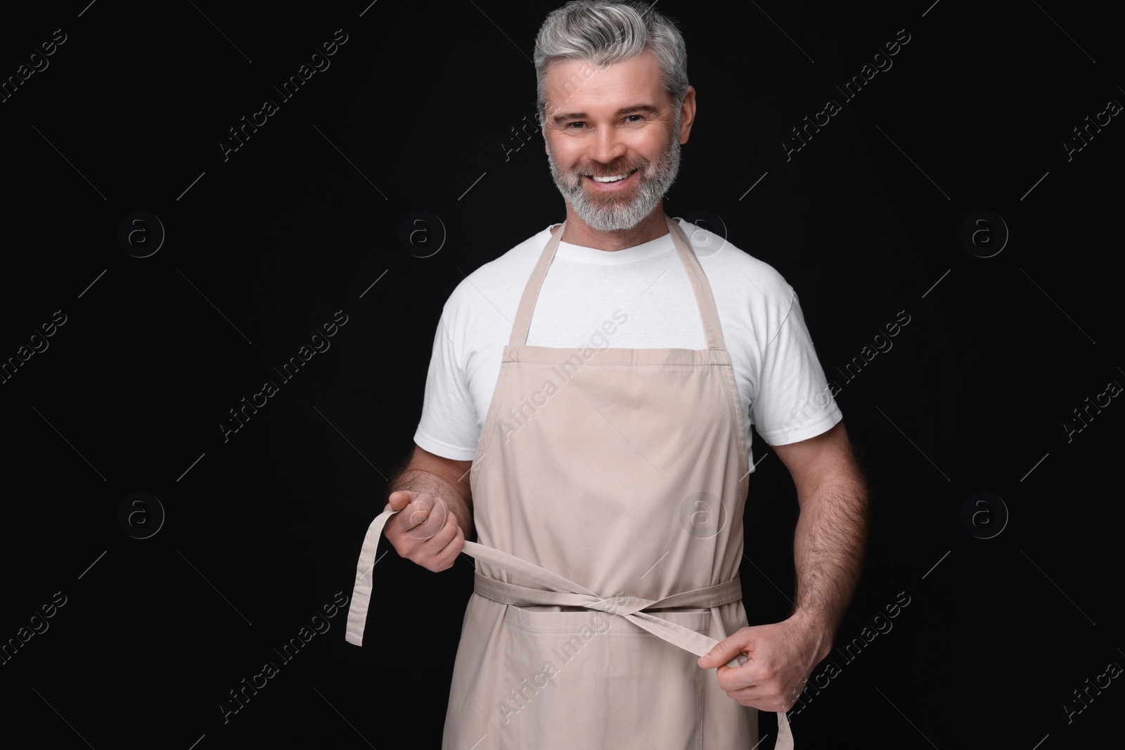 Photo of Happy man wearing kitchen apron on black background. Mockup for design