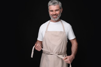 Happy man wearing kitchen apron on black background. Mockup for design