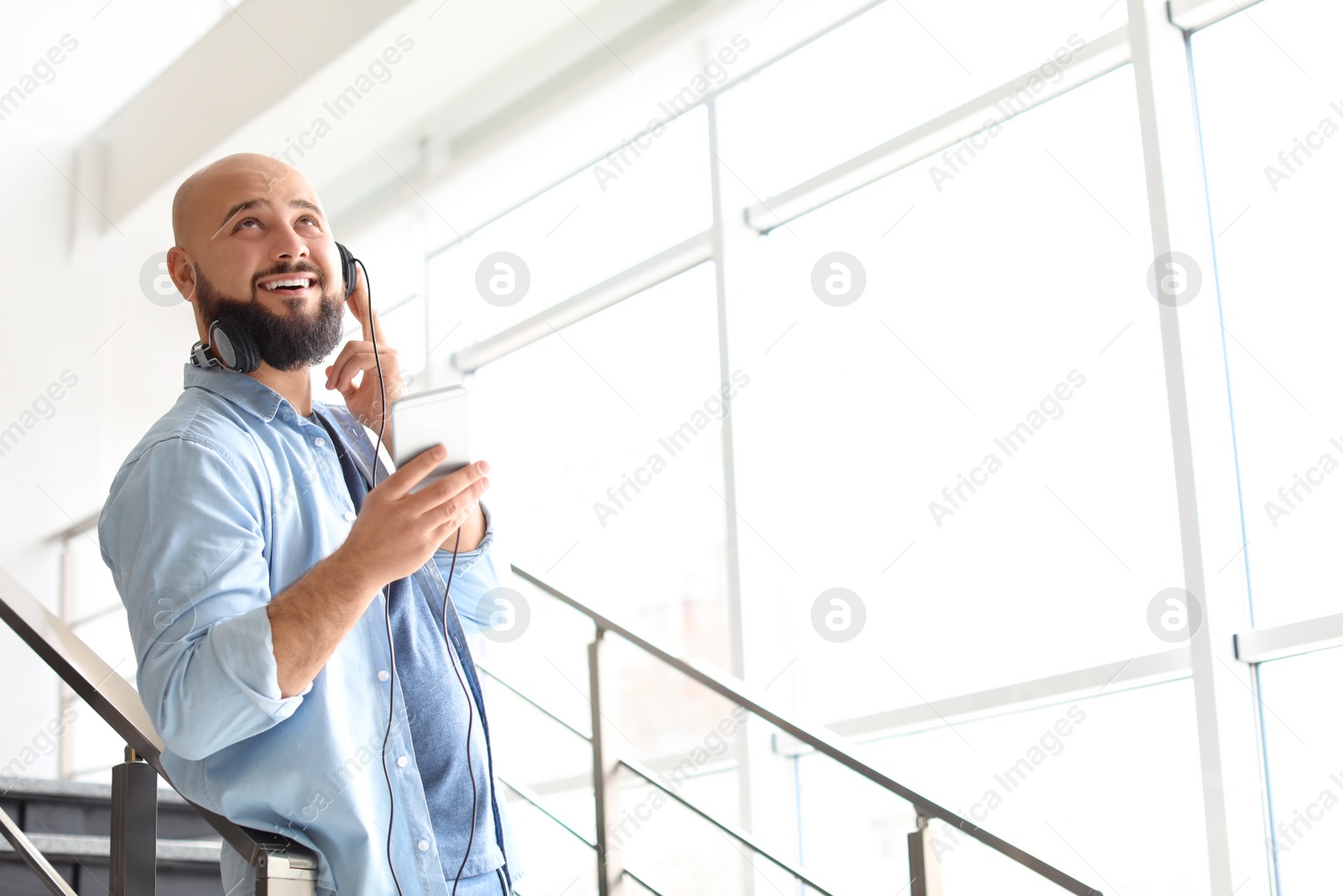 Photo of Portrait of young man with mobile phone and headphones on stairs