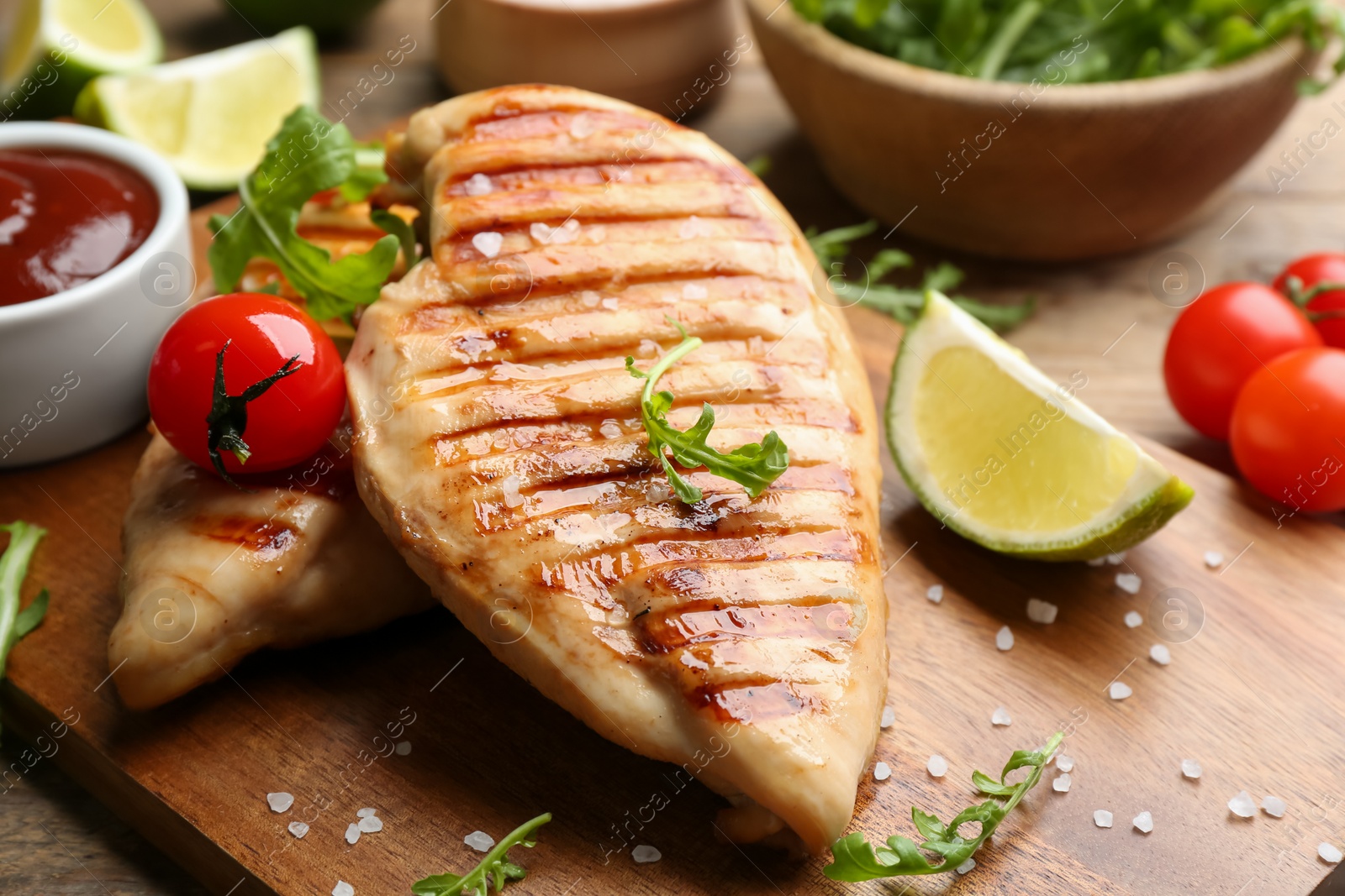 Photo of Tasty grilled chicken fillets with tomato and lime on wooden board, closeup