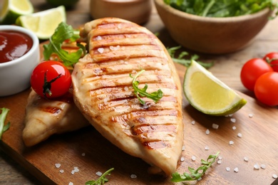 Tasty grilled chicken fillets with tomato and lime on wooden board, closeup
