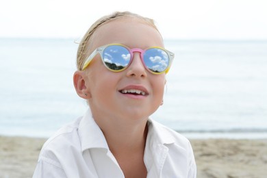 Photo of Little girl wearing sunglasses at beach on sunny day