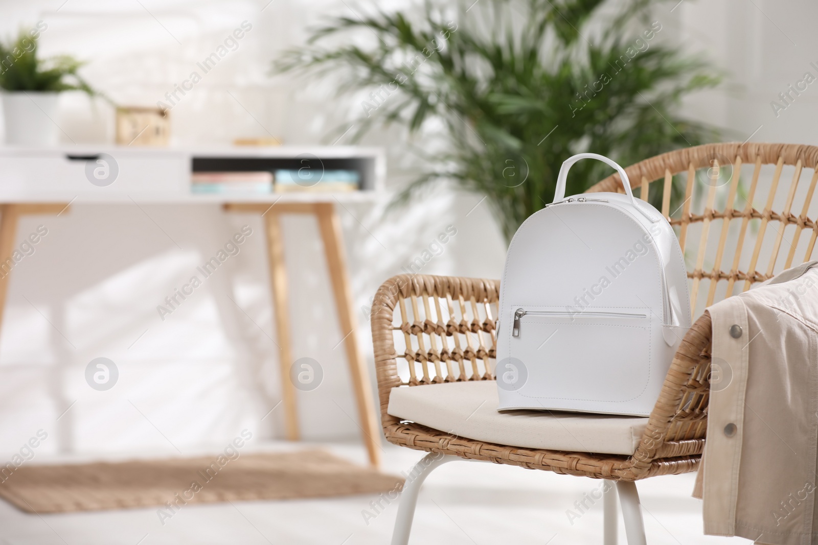 Photo of Stylish white backpack and jacket on wicker chair indoors, space for text