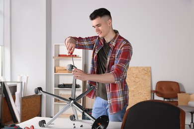 Young handyman repairing desk chair in room