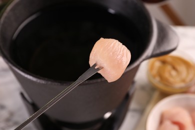 Photo of Fondue pot, fork with raw piece of meat and mustard on table, closeup