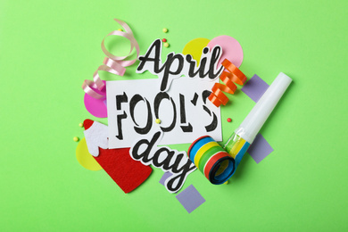 Flat lay composition with words APRIL FOOL'S DAY and party items on green background