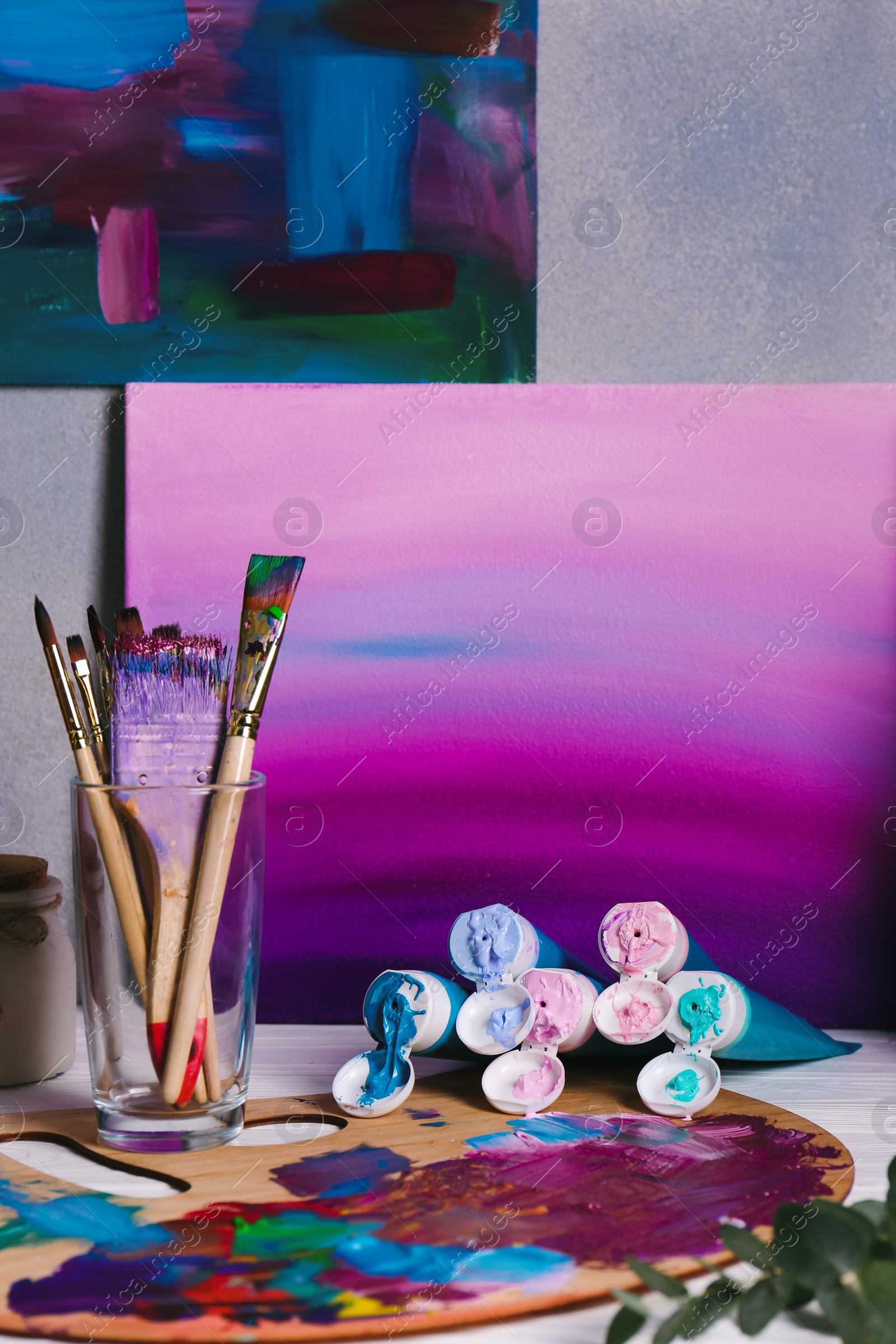 Photo of Canvas with gradient painting, brushes in glass and wooden artist's palette on table