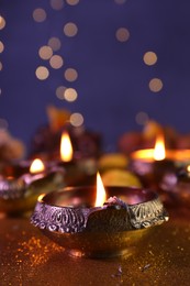 Photo of Diwali celebration. Diya lamp on shiny golden table against blurred lights, closeup