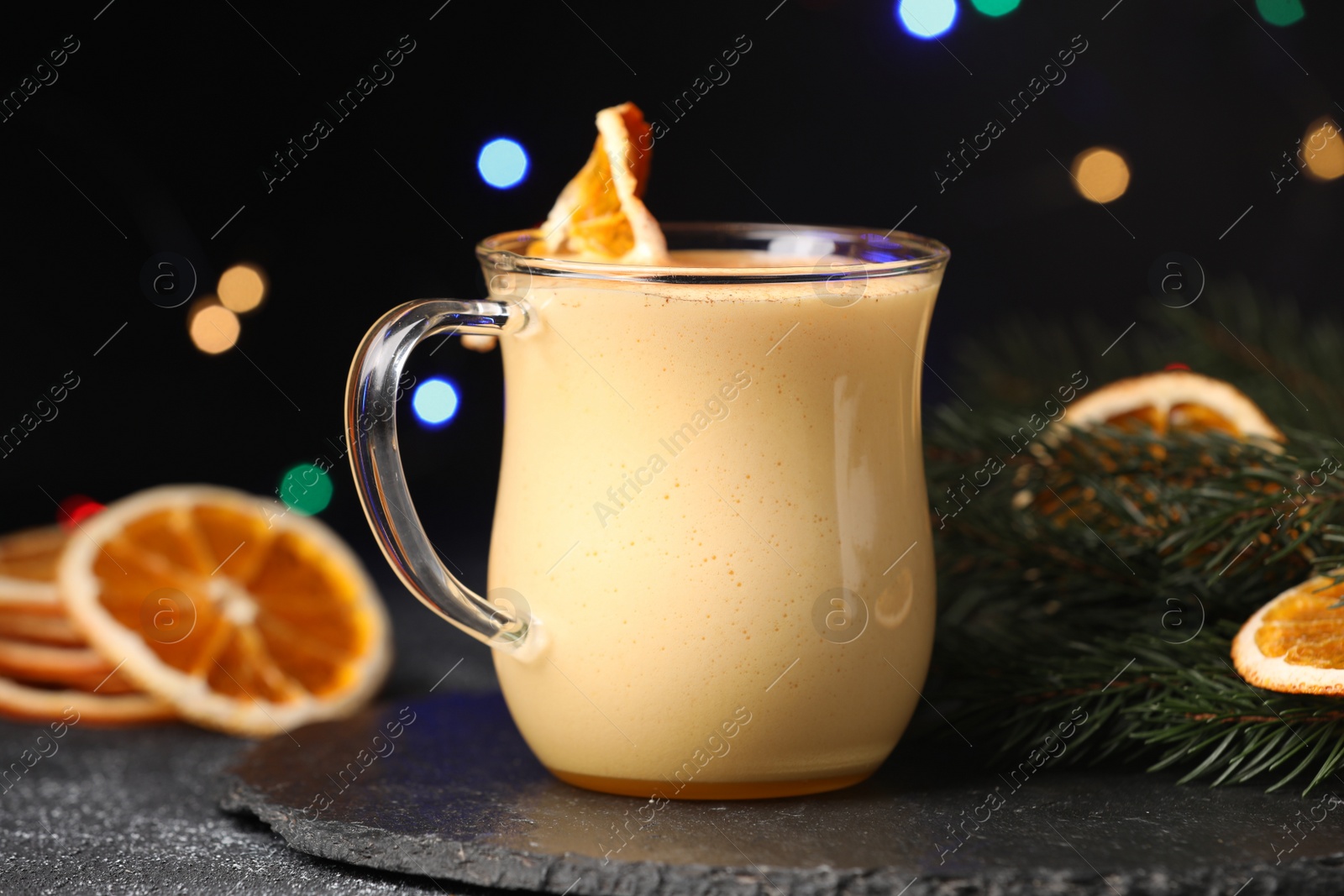 Photo of Glass cup of delicious eggnog with dried orange slice on black table