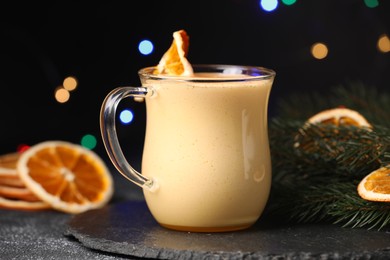 Photo of Glass cup of delicious eggnog with dried orange slice on black table