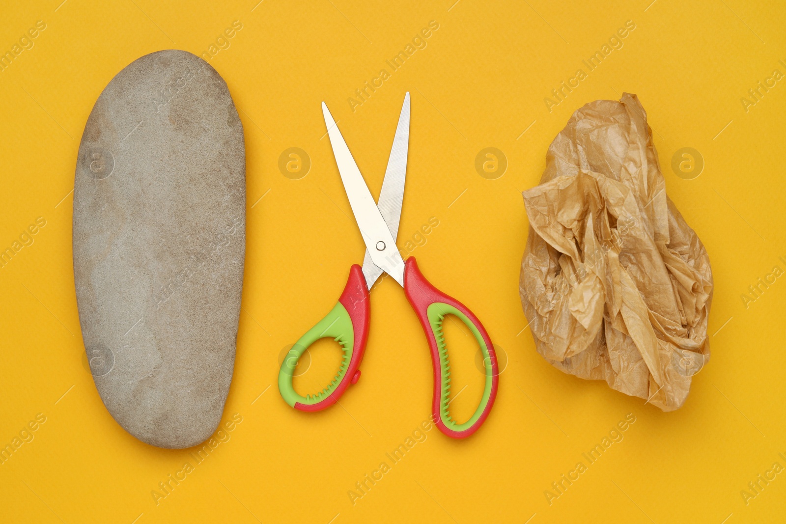 Photo of Rock, crumpled paper and scissors on orange background, flat lay