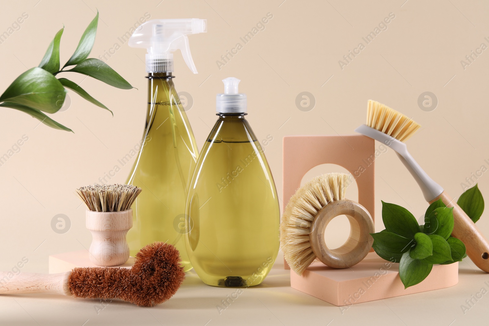 Photo of Bottles of cleaning product, brushes and floral decor on beige background