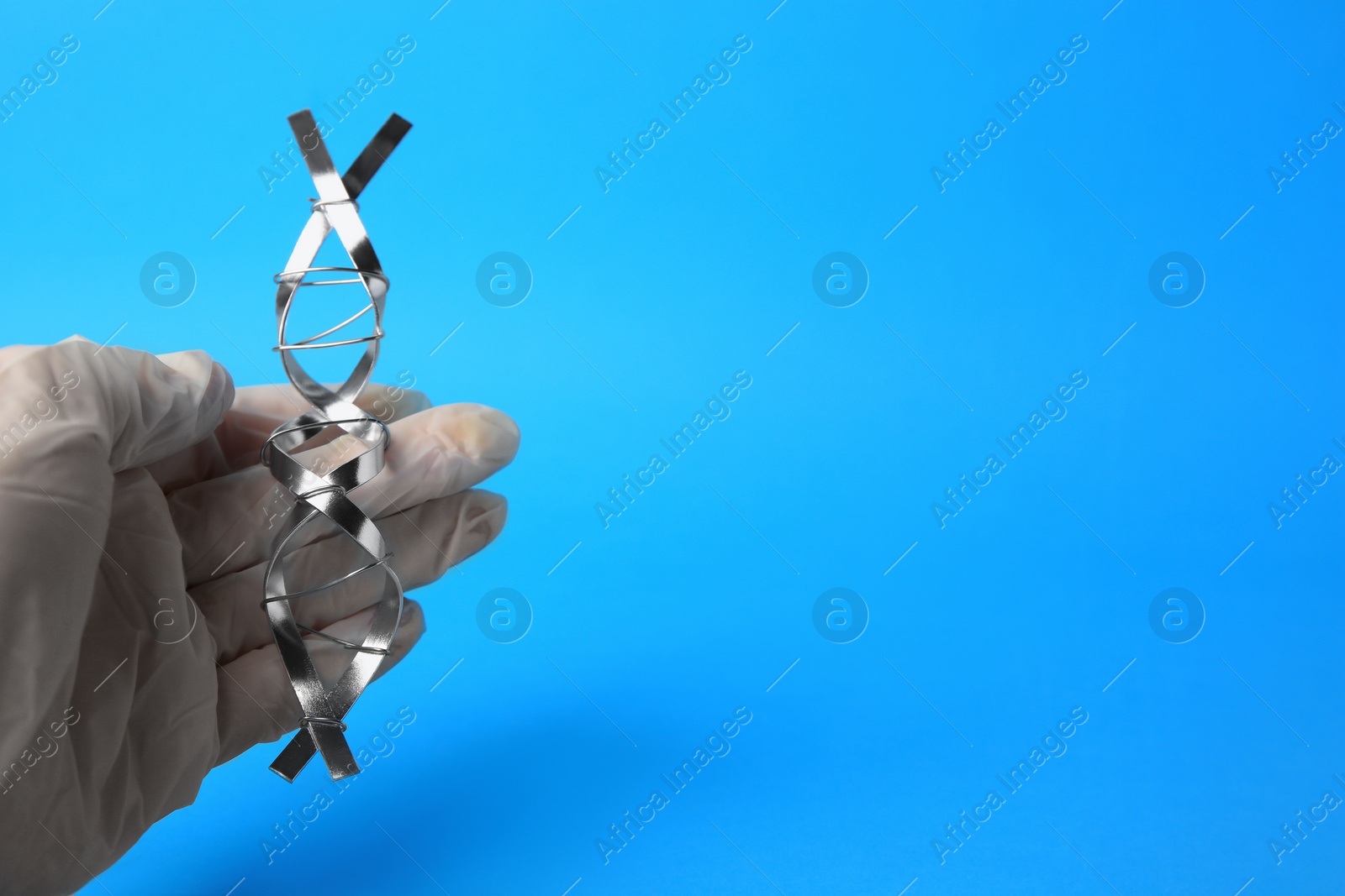 Photo of Scientist with DNA molecular chain model made of metal on blue background, closeup. Space for text