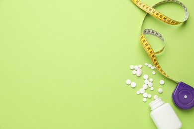 Photo of Jar of weight loss pills and measuring tape on green background, flat lay. Space for text