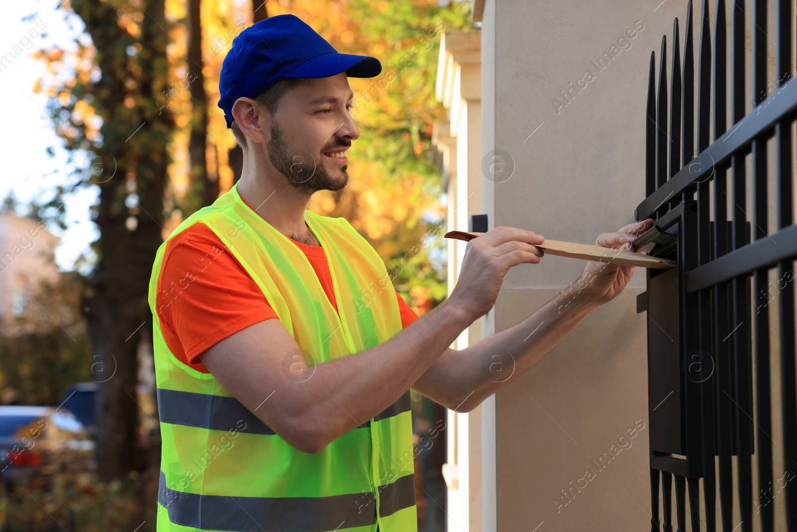 Photo of Courier in uniform dropping package into mailbox outdoors