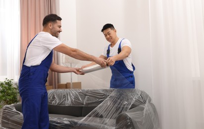 Photo of Workers wrapping sofa in stretch film indoors. Space for text
