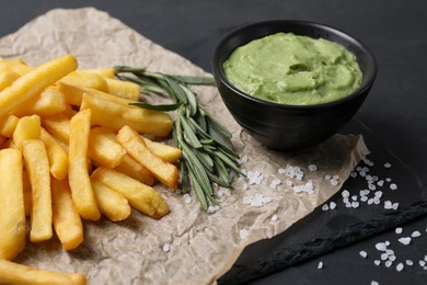 Photo of Serving board with french fries, guacamole dip and rosemary on black table, closeup