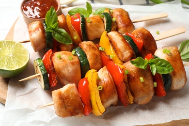 Delicious chicken shish kebabs with vegetables and lime on wooden board, closeup