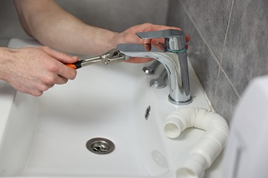Photo of Plumber repairing metal faucet with spanner in bathroom, closeup